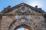 Bordeaux. Porte Dijeaux.<br> De ce coté, le triangle est occupé par les symboles royaux, couronne et fleurs de lys, mais aussi deux ailes, un casque et un poisson. Sous le triangle une tête animale surplombe le chiffre 1748 qui correspond à la date de sa construction.
