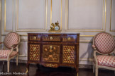 Musée des Arts Décoratifs. Salon de compagnie<br> La commode est un meuble d’ébénisterie parisienne, vers 1775, caractéristique du style Transition Louis XV-Louis XVI : façade et montants rectilignes associés à un tablier légèrement chantourné et des pieds en console. La très riche et élégante marqueterie d’essences variées en réseau de cubes, frise d’entrelacs, bouquet, a été restaurée par l’AFPA de Chartres en 2002. Sur le marbre, la pendule, en bronze doré, est une allégorie des Arts ; cadran signé Lemoyne à Paris, XVIIIème siècle.