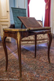 Musée des Arts Décoratifs. Salon de compagnie<br> Une table liseuse, vers 1750, par Pierre Migeon (1696-1758). Placage de bois de violette et bois de rose, et bronzes dorés. Ce meuble à transformation est caractéristique de la manière de Migeon : forme rognon, pieds élégamment cambrés à cinq pans, soulignés de filets de bronze ; dessus sur chevalet à crémaillère à inclinaison réglable ; deux abattants latéraux découvrant des casiers profonds ; tablette frontale formant écritoire doublée au revers d'un miroir ; petit casier postérieur contenant un écran roulé qui maintenu dressé protège le visage de la chaleur du feu. Une table liseuse semblable par son mécanisme a été réalisée pour Mesdames, filles de Louis XV.