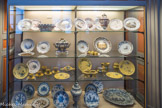 Musée des Arts Décoratifs. Deuxième antichambre. <br> Marseille. Grand feu. Le grand plat dont l’aile chantournée est en relief dans le goût de Savone, illustre la production en camaïeu bleu de la première manufacture, Saint-Jean-du-Désert, vers 1700, de même le pot de pharmacie dont le décor ne couvre que la partie visible, quand il est présenté sur l'étagère de l’apothicairerie (étagère du bas)
L'assiette en camaïeu bleu, appelée « à la Camargo » à cause de son sujet inspiré d'une gravure d’après Nicolas Lancret, représente la célèbre danseuse belge Melle de Camargo ; on peut y lire des couplets en l'honneur du vin et de la table (étagère du bas à gauche).
Petit feu. Dans la seconde moitié du XVIIIème siècle, en rivalité serrée avec la porcelaine grâce à l'adoption du petit feu, les célèbres manufactures de la Veuve Perrin, de Gaspard Robert, Savy, Bonnefoy, affectionnent les décors de fleurs aux longues tiges souples librement jetées sur la surface de l'assiette, les paysages animés, les marines rappelant celles du peintre marseillais Lacroix, les trophées de poissons évoquant la « bouillabaisse ».
Joseph II Fauchier est sans doute l'inventeur des fonds jaunes, comme ensoleillés, qui connaîtront un grand succès dans toutes les fabriques du Midi.
Enfin, le goût de la ronde-bosse a entraîné une importante production de trompe-l'œil, appelés assiettes « à l'illusion » garnies de noix, d'amandes ou de pommes habilement modelées.