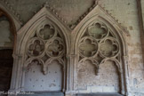 Saint-Emilion. L’ensemble Collégiale.<br> Le cloître. À l’est, trois enfeus furent placés dans l’épaisseur du mur. Le premier est de style analogue à ceux du Sud. Les seconds, d’un dessin presque identique, sont formés deremplages où trois quatrefeuilles sont inscrits dans des cercles formés par un tore. C’est là un tracé habituel aux baies du XIVe siècle 
Un de ces enfeus a conservé une  partie de son décor peint, conçu en fonction du cadre architectural- : un Christ, dont la tête est entourée du nimbe crucifère, fait un geste de bénédiction. Il domine: la Vierge, à longs cheveux blonds, tenant un sceptre terminé par un fleuron et un saint, jeune, assis symétriquement à 1a Vierge et qui est peut-être saint Jean.
Le style de ces peintures, malgré leur mauvais état de conservation, peut être attribué à la première moitié du XIVe siècle.