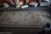Musée d'Aquitaine. <br> Mosaïque d’une maison d’habitation urbaine.
Bordeaux, rue Père-Louis-de-Jabrun en 1876 VIe siècle ?
Terre cuite, calcaires, marbres.
Ce pavement de mosaïque de taille impressionnante ornait plutôt une galerie que la salle de réception d’une habitation urbaine (domus), car on a retrouvé en bordure d’un des longs côtés un aménagement avec une base de colonne en marbre encore en place. Lors de sa découverte en 1876, la mosaïque mesurait plus de dix mètres de longueur, mais les mauvaises conditions de conservation (sol vaseux et instable) n’ont pas permis à l’époque d’en déposer l’intégralité. Elle se prolongeait encore considérablement au sud sous les maisons actuelles, non loin de l’extrémité du port antique qui pénétrait profondément dans la ville. De l’autre côté, au nord, d’autres pavements de types très différents appartenant à la même demeure ont été découverts en 1973-1974 lors de fouilles sous l’îlot Saint-Christoly. On peut imaginer l’impression grandiose ressentie à l’époque par les visiteurs qui, fraîchement débarqués du port, s’arrêtaient chez ces riches propriétaires installés au cœur de la ville antique...
Le tapis de la mosaïque reprend une composition d’octogones entourés de carrés séparés entre eux par des losanges. Comme le reste du pavement, les interstices sont comblés de motifs géométriques (pavés carrés, demi-roses, losanges et écoinçons) extrêmement colorés dont l’influence africaine se fait nettement sentir, notamment la Tunisie (station thermale antique de Djebel Oust). Les couleurs dominantes sont le blanc, le noir, le rouge, le jaune et le vert. Elle est encadrée d’une frise à dents de loup et terminée sur un côté par une élégante frise de rinceaux à feuilles de lierre, rare en Aquitaine.