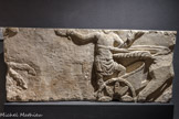Musée d'Aquitaine. <br> Relief de course de char.
Original : Bordeaux, place du Palais-de-l’Ombrière, en 1842, en remploi dans la base du rempart romain ?
Époque romaine.
Fac-similé.
Ce relief présente un aurige sur un char tiré par deux chevaux (bige) dont il ne subsiste que l’arrière-train. L’homme est vêtu d’une courte tunique sans manche et d’une sorte de cuirasse (lorica) qui lui protège le torse. Les rênes autour du corps, il exécute son tour triomphal tenant la couronne et la palme, trophées du vainqueur. Un second char, dont il ne reste que la tête et les pattes antérieures d’un cheval, suit le premier. Ce relief a pu orner un mausolée : le thème du vainqueur est souvent utilisé comme symbole funéraire (accès dans l’au-delà).