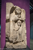 Musée d'Aquitaine. <br> Stèle funéraire d’une fillette
Bordeaux, 7 bis rue Guillaume-Broçhon en 1831, en remploi dans la base du rempart romain Fin du Ier siècle Calcaire
Sur cette stèle découverte en 1831, une fillette décédée prématurément est représentée de face et en pied (debout), selon le modèle grec adopté au début de l’époque romaine, mais dans une niche en cul-de-four, généralement utilisée par les Romains. L’usage étant de faire figurer aux côtés du défunt ce qui lui était particulièrement familier au cours de sa vie et représentatif de sa position dans la société, la fillette est accompagnée des animaux qu’elle chérissait. Le coq mordillant la queue du chien que l’enfant tient dans ses bras ajoute au pittoresque de la représentation une touche vivante et assez émouvante.
La coiffure, le vêtement, ainsi que les oreilles percées pour des boucles d’oreilles métalliques (aujourd’hui disparues) indiquent que l’enfant est une fillette. Elle est coiffée selon la mode de l’époque : elle a les cheveux courts, avec deux mèches bouclées sur les tempes. Un élégant manteau recouvre sa longue tunique aux plis fins, sous lesquels apparaissent les pieds chaussés de l’enfant.
La stèle étant brisée sur un côté, la dédicace ne peut être entièrement restituée. Le prénom de la fillette, qui devait se situer juste après l’invocation aux dieux Mânes (D. M), demeure inconnu. Le seul nom inscrit, LAETVS, est probablement le prénom du père (PAT.).
D(IIS).M(ANIBVS).[.	..]/
PAT(ER) [...]
« Aux dieux Mânes ... Laetus ... son père ... ».