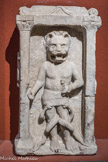 Musée d'Aquitaine. <br> Autel léontocéphale : Mithra-Chronos à tête et « pieds » de lion. Fin du IIe siècle – 1er moitié du IIIe siècle.
La très haute teneur symbolique du relief contraste fortement avec le cadre conventionnellement gréco- romain de l'autel à niche et pilastres sur les côtés, aiguière et patère à libation sur les faces latérales. Le léontocéphale présente, quant à lui, un certain nombre d'éléments originaux par rapport à ceux qui ont été retrouvés dans les autres mithrea (temples du dieu Mithra) du monde romain : il se tient déhanché, avec deux serpents à tête de dragon qui s'enroulent autour de ses jambes en une spire et demie chacun. La représentation de sa tête gueule grande ouverte découvrant des canines menaçantes était destinée à impressionner les fidèles. La représentation habituelle présente un seul serpent enroulé en trois ou six circonvolutions pour symboliser la course apparente du soleil d'un solstice à l'autre.
Le lion représente le quatrième des sept grades d'initiation aux mystères de la religion mithriaque, dont la clef permet d’ouvrir symboliquement les portes, notamment lors de la cérémonie commémorant la naissance de Mithra qui marque, comme pour Janus, le début de la nouvelle année. Les Grecs et les Romains à leur suite, assimilèrent ce dieu à Kronos ou Chronos par une mauvaise compréhension du nom oriental qui le désigne. Ils en firent donc un dieu du temps (« chronos » en grec). Son élément est le feu. ce qui implique l'utilisation du miel et non de l’eau pour la purification précédent la-célébration. Des ail peintes ont pu figurer au fond de la niche, puisque de nombreuses sculptures représentent le léontocéphale ailé.
Calcaire.