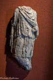 Musée d'Aquitaine. <br> Statue de Cautopatès.
Bordeaux, fouilles 146 cours Victor-Hugo en 1986 Fin du IIee siècle - lère moitié du IIIe siècle Calcaire.
Cautopatès est, avec Cautès, l’un des deux compagnons de Mithra, dieu dont le culte, d’origine orientale, connut un essor considérable dans tout l’Empire romain à partir de la fin du IIe siècle et s’éteignit, concurrencé par le Christianisme, au cours du IVe siècle. Bien que tendant vers le monothéisme, ce culte à mystères pénétré d’astrologie comprend des rites d’initiation et une célébration - sacrifice du taureau et repas rituel - tout à fait particuliers. Il est honoré dans des grottes ou des sanctuaires enterrés, et seuls les hommes y sont apparemment admis.
Il célèbre la lumière et la force, et prône des valeurs telles que fraternité, égalité et loyauté qui le firent particulièrement apprécier des soldats, mais aussi des commerçants et des voyageurs pénétrés de ces rites adoptés en Orient, des artisans, des affranchis, et des esclaves qui y retrouvaient en quelque sorte une famille.
La statue de calcaire retrouvée en 1986 dans le temple (mithraeum) de Bordeaux présente Cautopatès selon l’usage : il est habillé à l’orientale comme le dieu Mithra lui-même, avec le bonnet phrygien et la cape colorés de rouge. Contrairement à son compère Cautès qui, debout, jambes croisées, tient sa torche levée et symbolise la lumière, le jour, le renouveau..., Cautopatès, torche baissée, représente en symétrie le crépuscule, l’automne, ...la mort. Tous deux devaient encadrer l’illustration du sacrifice du taureau par Mithra (tauroctone). Des traces de fixation subsistent d’ailleurs au bras et à l’épaule de Cautopatès.