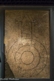 Musée d'Aquitaine. <br> Mosaïque dite du « Saint Sépulcre » (Anastasis)
Bordeaux, fouilles des allées de Tourny en 1971 Fin IVe siècle - début Ve siècle Tesselles de marbre, calcaire et terre cuite
Ce pavement de mosaïque a été retrouvé lors des fouilles des Allées de Tourny en 1971, recouvert par une autre mosaïque blanche et noire à très petites tesselles (cubes de mosaïque). C’est ce qui explique que la surface en a été bûchée de façon à permettre au lit de mortier dé la mosaïque située au-dessus d’adhérer.
Le dessin ornant ce pavement-ci est réalisé avec quelques tesselles de terre cuite, de calcaire jaune et surtout de marbre noir, dans un mortier fait de chaux et de briques concassées qui procure à l’ensemble cet aspect rosâtre : c’est l’opus signinum.
On reconnaît le plan d’un édifice circulaire (« plan centré ») à déambulatoire surmonté par le dessin en perspective d’une construction dont on voit les deux gâbles, chacun sommés d’une croix. Au-dessous, une voûte est suggérée par deux arcs en plein cintre qui semblent ceux d’une charpente apparente avec ses poutres horizontales (« entraits »). Il s’agit donc d’un édifice religieux, peut-être la basilique du Saint-Sépulcre à Jérusalem érigée au milieu du IVe siècle par l’empereur Constantin récemment converti au christianisme, car le plan adopté pour l’Anastasis (sanctuaire de la Résurrection) destiné à recouvrir le tombeau vide du Christ est, conformément à la tradition romaine des mausolées princiers, de forme circulaire. L’hypothèse se trouve confortée par le fait que ce sanctuaire embrasa l’imagination de tous en Occident et suscita, à l’instar de la propre mère de l’empereur, de nombreux pèlerinages et notamment celui de Bordeaux à Jérusalem, dont nous avons le récit, effectué par un Aquitain en 333, avant même que ne soit achevée la construction de l’église du Saint-Sépulcre dédicacée deux ans plus tard.