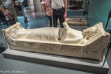 Musée d'Aquitaine. <br> Gisant d’Aliénor d’Aquitaine.
Fac-similé
Ce gisant, conservé à l’abbatiale de Fontevrault (Maine-et-loire), est daté entre 1210 et 1215. Inhumée à l’abbaye de Fontevrault où elle avait terminé sa vie, Aliénor y est entourée de son second mari Henri Il Plantagenêt, de leur fils Richard 1er Cœur de Lion (tous deux ducs d’Aquitaine et rois d'Angleterre) et de leur fille Jeanne.
Le gisant placé sur le tombeau Représente l'image de la défunte sur son lit de mort : Aliénor tient un livre dans ses mains, bien qu’elle semble plutôt assoupie. Décédée à plus de 80 ans, le temps paraît l’avoir épargnée, et son expression est empreinte de sérénité.
La sculpture originale comporte encore les traces de peinture (bleue et blanche pour son vêtement, rouge pour le drap), non reproduites ici. Figure historique marquante de l'Aquitaine, mais aussi de la France, de l’Angleterre et de l’Occident médiéval, Aliénor joua également un grand rôle dans la diffusion de la poésie courtoise et fût ainsi considérée comme la « reine des troubadours ».