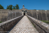 Citadelle de Blaye<br>. Le pont dormant. Au cours du XVIIe siècle, l’ancienne cité fortifiée médiévale est progressivement confortée par plusieurs campagnes de travaux. Ces dernières marquent la volonté du gouvernement de transformer Blaye en une important place forte militaire. Sa création s'accompagne de la venue d’une nombreuse garnison qui, avec son administration, envahit l’ancienne cité.
En 1680, l’ingénieur Ferry est l’auteur du premier plan systématique de reconstruction de la citadelle. Son Mémoire reçoit un commencement d’exécution. Cependant en 1685, Louis XIV confie le projet définitif à Vauban. Ce dernier applique son principe de fortification bastionniée. Dès lors, les lieux entièrement fortifiés deviennent place forte avec arsenal et casernement.
Vauban adapte toujours ses constructions aux conditions de chaque lieu. Ici, à Blaye, il utilise le promontoire côté fleuve, et absorbe ingénieusement les lignes défensives déjà existantes côté terre, intégrant les fortifications médiévales préexistantes. Deux entrées en commandent l’accès : la porte Royale, à l’est, et ici, au sud, la porte Dauphine.