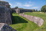 Citadelle de Blaye<br>. Dans sa configuration actuelle, la citadelle apparaît comme un ensemble hémicylindrique formé d'une enceinte à quatre bastions et trois demi-lunes, ceinturé par de profondes douves et par un glacis. Les demi-lunes, de forme triangulaire, sont conçues afin de protéger les courtines et les entrées de la citadelle. Celles-ci sont au nombre de deux : la porte royale et la porte dauphine, lesquelles sont précédées de ponts dormants en pierre. Ceux-ci sont le résultat d'une campagne de modernisation de la citadelle intervenue dans la seconde moitié du XVIIIe siècle : celui de la porte dauphine date de 1770, tandis que celui de la porte royale date de 1780. Auparavant, la citadelle était équipée de ponts-dormants en bois, matériau jugé trop peu fiable en cas d'attaque. L'intérieur de la forteresse forme une véritable 