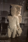 Le Fâ Barzan. <br> Au sein d’un de ces îlots bâtis caractérisés par de nombreuses et riches constructions couvrant plusieurs milliers de m2, une sculpture en calcaire d’une divinité juvénile ailée a été mise au jour Elle semble avoir été remployée comme support d’un probable pilier en bois au sein d’un aménagement d’époque tardive.
Conservée sur 66 cm de hauteur, l’œuvre fut vraisemblablement réalisée par un artiste local du 1er ou Ile siècle de notre ère. Mutilée, elle fit l’objet de déprédations dès l’Antiquité.
Le personnage est représenté adossé à un chêne, ailes déployées. Son bras droit n’est pas parvenu jusqu’à nous. Sa main gauche repose en un geste protecteur sur un volatile se tenant debout à ses côtés, vraisemblablement un aigle. Cet oiseau traduit-il la présence du Dieu Jupiter ?
