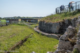 Le Fâ Barzan. <br> Le sanctuaire.
L'aire sacrée du sanctuaire est délimitée par un péribole qui la sépare de l'espace profane des rues périphériques. Le sanctuaire du Fâ couvre une surface rectangulaire de 12000 m2. La galerie à portique sud est longue de 119.40 m pour une largeur interne de 5.60 m, soit environ 670 m2. Les maçonneries ne sont connues qu'en fondation. Les murs sont construits avec :
• des appareils rectangulaires (18 cm sur 9 cm) en parement d'un noyau en béton, avec des joints marqués au fer ;
- des moellons sommairement équarris sur les parements non visibles.
L'intérieur de la galerie et de la cour est comblé par un remblai calcaire de 0 à 2,50 m de hauteur qui compense la pente de l'ancien sanctuaire et correspond au niveau de circulation de la nouvelle aire sacrée.
Ces constructions ont été reconstituées, à l'angle sud-ouest, sur la base des observations archéologiques. Un rang d'ardoises sépare les constructions antiques des reconstitutions.
Pour la partie ouest de cette galerie, partiellement connue en fouille, il a été choisi de représenter le péribole à l'aide de gabions posés à l'aplomb des vestiges. Les dés calcaires correspondent à l'emplacement des bases de colonnes de ce portique. La surface de pose était horizontale dans l'Antiquité. Les paliers formés par les gabions correspondent à la déclivité actuelle du site.