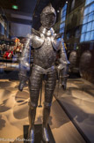 <center></center><center>Les Invalides. </center> Armure dite d'Henri II. ». Atelier Français.
Vers 1550.
Le thème général du décor repoussé et ciselé de cette armure est la rivalité entre César et Pompée, la défaite de ce dernier à Pharsale, sa fuite en Egypte où il est assassiné et l’envoi de sa tête à César. Plusieurs détails de cette ornementation virtuose ont été repris par Etienne Delaune sur des estampes exposées ici. Le décor poli au blanc, sans aucun apport de dori^e, de damasquinure ou de noirci a laissé penser que cette pièce serait restée inachevée après la mort accidentelle d’Henri II. Aucun élément emblématique et sources documentaires précises (il n’a intégré les collections de la Couronne qu’en 1671) ne prouvent cependant l’appartenance de ce harnois au souverain.