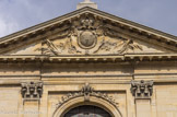 <center></center><center>Notre-Dame-des-Victoires. </center>Le portail est couronné par un fronton triangulaire avec au tympan, un écusson aux armes de la France surmonté de la couronne royale et entouré du grand cordon du Saint-Esprit. Pilastres d'ordre corinthien.