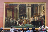 <center>Sacre de l'empereur Napoléon Ier et couronnement de l'impératrice Joséphine dans la cathédrale Notre-Dame de Paris, le 2 décembre 1804, 1806-1807. </center>Louis DAVID. Salon de 1808. Aussi beau que Rubens ! », disait Géricault parlant du Sacre. Cette page immense procède en effet du Couronnement de Marie de Médias de Rubens (Louvre, galerie Médicis). Mais ici, l'animation baroque fait place a un parti pris de rythmes verticaux qui donnent à l'œuvre M solennelle grandeur. David use avec une maîtrise consommée de procédés nouveaux pour lui : éclairage contrasté groupant des masses heureusement distribuées, empâtements, coloris sonore, qui font de cette page d'histoire, de ce document officiel, une merveilleuse fête pour l'œil. David avait d abord représenté Napoléon (cambré) se couronnant lui-même : on en distingue les traces (couronne, profil) sur la toile, en arrière de la figure actuelle (redressée) de l'Empereur, qui s apprête à couronner Joséphine. Dans cet espace, David a ajouté un ecclésiastique dont les traits sont ceux de Jules César, et dont le regard d aigle est fixé sur le nouvel empereur... Destiné à la postérité, le tableau corrige l'histoire : ainsi, la mère de Napoléon, qui n'avait pas voulu assister au sacre, figure au centre de la composition, parmi les 191 personnage réels ou imaginaires qui peuplent cette toile, seule rivale au Louvre des Noces de Cana de Véronèse par sa taille.