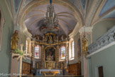 <center>Hauteluce : Église Saint-Jacques-d'Assyrie.</center> A gauche, la croix de bois sculptée à la main date de 1723. Le retable baroque s’inscrit dans une abside à sept pans en insérant des verrières dans les volets latéraux, ce qui lui donne une allure bien particulière, très aérée. Il a été réalisé en 1749 par Joseph Albertini, de la Valsesia (vallée entre Turin et Milan) et Joseph Gentil, originaire de Macôt en Tarentaise.
